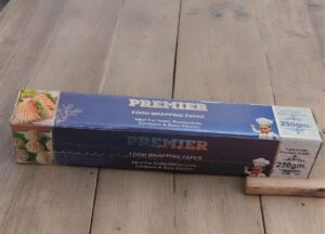 Blue Premier food wrapping paper box on a wooden table, with sandwich images on the side.