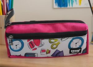 Pink pencil case with a white front panel featuring colorful clocks and school supplies on a wooden desk surface.