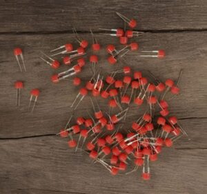 Assorted red LED components with two leads scattered on a wooden surface.