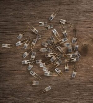 Loose clear LEDs with two leads scattered on a wooden surface.