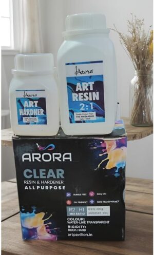 Two white bottles labeled Art Resin (2:1) and Art Hardner sit on a colorful ARORA CLEAR box, with dried flowers in a jar in the background.