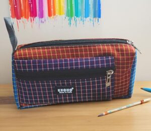 Colorful fabric pencil case with a rainbow grid pattern, zipped top, on a wooden desk with two pencils nearby.