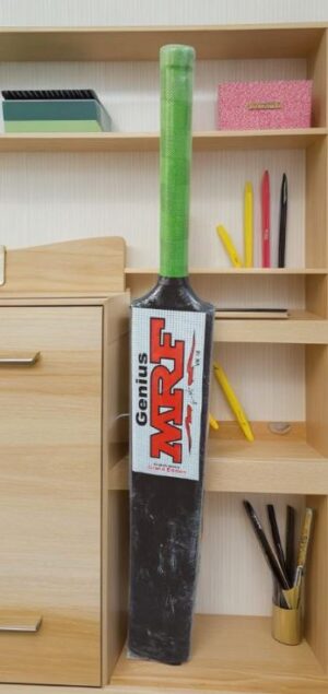 Tall black cricket bat with a bright green handle leaning against a wooden shelf, label reads 'Genius MAX'.