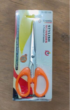 Orange-handled scissors in blister-pack packaging on a wooden surface, labeled 'STYLISh SCISSORS' for Akoty/Cramly brand