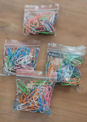 Five resealable plastic bags filled with colorful paperclips scattered on a wooden table.