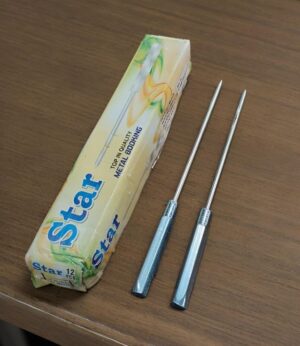 Two stainless steel dental probes with blue plastic handles beside a Star brand box on a wooden table.