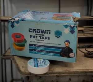 Box of Crown PVC tape with rolls of tape beside it on a workbench shelf in a workshop