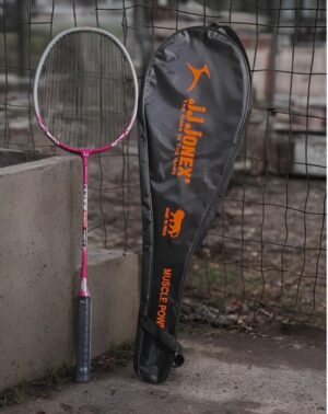 Pink tennis racket with a dark grip leaning against a concrete block beside a black sports bag with orange lettering and logo.