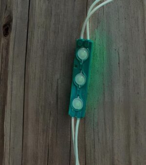 Teal three-LED module with white wiring on weathered wood surface.
