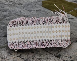 A row of LED modules with pink and white wires laid on a rough stone surface, forming a bundled strip array.
