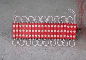 Row of red firecrackers with white fuses laid in a line on a gray surface.