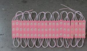 Row of pink plastic modules with circular contact dots and looped white cords, laid on a gray surface.
