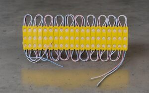 Row of yellow LED modules wired together with pink and blue leads on a concrete surface.