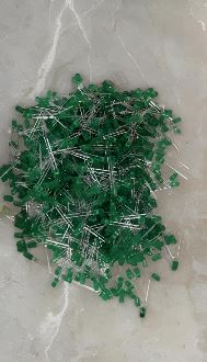 Pile of small green glass seed beads with silver pins scattered on a light gray surface.