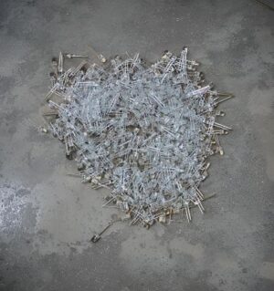 Pile of broken glass tubes with metal caps scattered on a concrete floor.