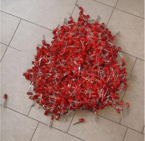 Pile of red LED light diodes with metal leads scattered on a tiled floor, showing multiple components.