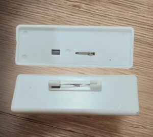 Two white plastic cases opened, revealing a small metal tweezer-like tool and a blade on a wood surface.