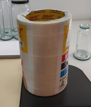 Large roll of SunJet self-adhesive tape on a lab bench, with glass bottles in the background.