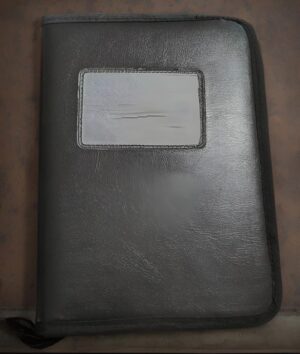 Black leather binder or portfolio with a small rectangular clear window on the front cover; the surface is textured and slightly worn.