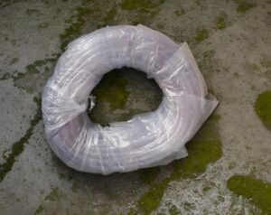 Large roll of clear plastic wrap lying on a mossy concrete floor.