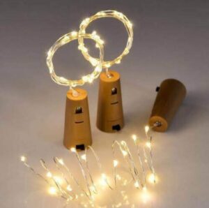Three small wooden peg dolls connected by warm white fairy lights, two standing with loops between them and one lying on its side, creating a playful decorative scene.
