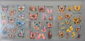 Collection of colorful butterfly stickers arranged on a frosted glass surface with flowers and handwritten phrases like 'Love you' and 'Happy Birthday'.