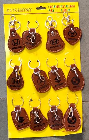 Set of leather-look keychains with car logos (Honda, Toyota, Hyundai, Suzuki, BMW) on a yellow display card, each with metal rings and brown stitching edge.