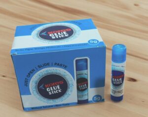 Blue Kore's Glue Stick box with a single glue stick on a wooden surface.