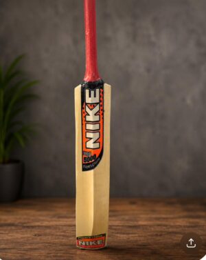 Cricket bat with red grip standing upright on a wooden floor, Nike branding visible on the blade.