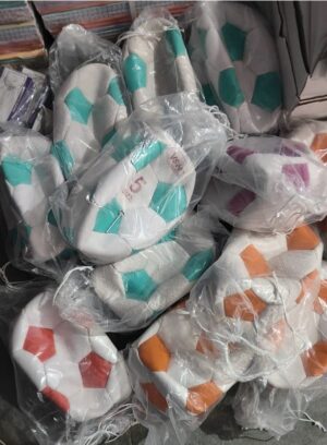 Assorted white cushions with teal hexagon patches, some with orange patches, all wrapped in plastic.