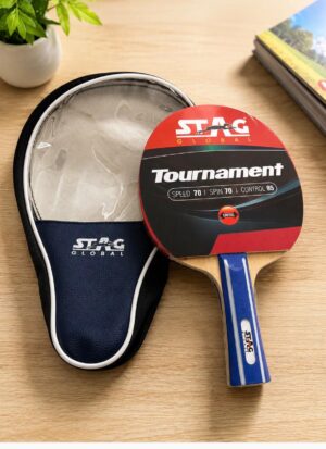 Table tennis paddle with blue handle and red/black branded rubber on a wooden table, next to a navy pouch labeled STAG Global.