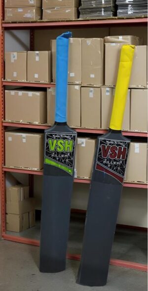 Two tall padded sports bats with blue and yellow handles leaning against red warehouse shelving, with stacked boxes in the background.