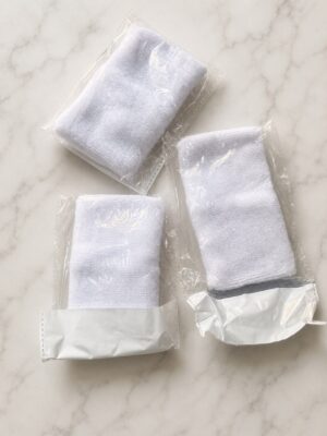 Three white towels in clear plastic packaging placed on a light marble surface.
