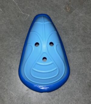 Blue plastic mask-like toy piece with two eye holes and a mouth hole placed on a gray concrete floor