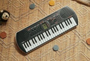Portable Casio keyboard lying on a patterned carpet with colorful coins scattered around it.