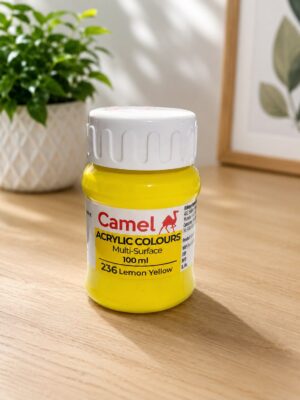 Yellow Camel acrylic paint bottle (Lemon Yellow) on a wooden table with a plant in the background.