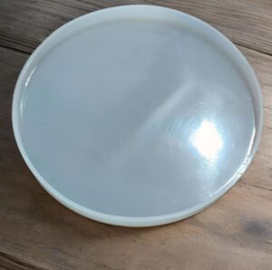 Round white plastic container lid with a translucent gray interior resting on a wooden surface, viewed from above