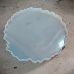 Round pale blue silicone baking mold with a scalloped edge, filled with pale liquid, resting on a concrete floor