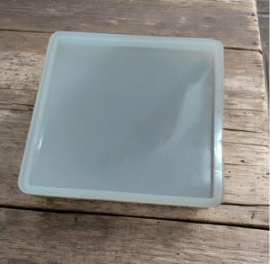 Light blue-rimmed square plastic tray with a translucent lid resting on a weathered wooden table.