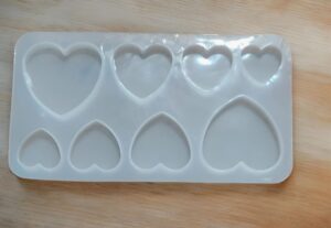 White silicone heart-shaped mold with eight cavities of varying sizes on a wooden surface