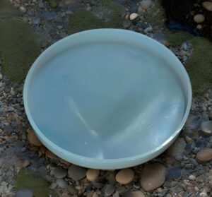 White round plastic basin filled with pale blue water on a pebble-covered beach.