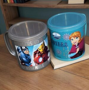 Two character-themed plastic mugs on a desk: gray Avengers (Iron Man/Captain America) mug beside a blue Frozen-Anna mug with a JOYO label.