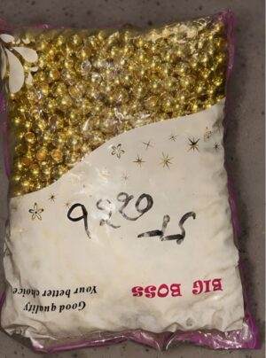 Bag of small gold craft beads in a pink-edged plastic package with a white label and handwritten numbers on it, intended for decorative crafts.