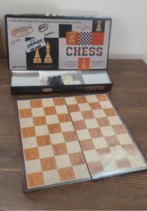 Open, double-sided wooden chessboard spread on a table with its packaged chess set visible in the background.
