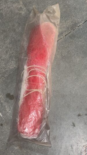 Red sausage wrapped in clear plastic with string tied around it, resting on a concrete floor.
