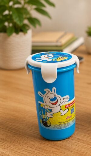 Blue plastic children’s lunch container with a white snap-on lid and a cartoon bunny on the label, placed on a wooden surface near books and a plant image in the background.