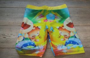 Colorful kids' swim trunks with smiling bear characters and a yellow waistband, laid flat.