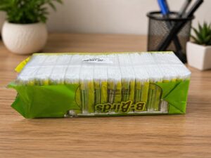 Pack of cotton swabs in green and yellow plastic wrap on a wooden desk.