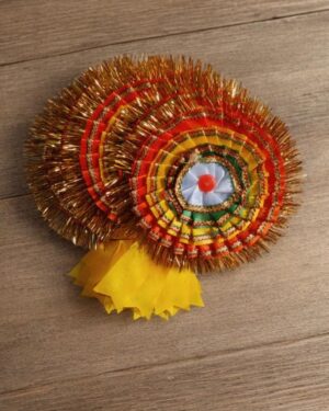 Colorful circular tinsel rosette with yellow ribbon tails on a wooden surface.