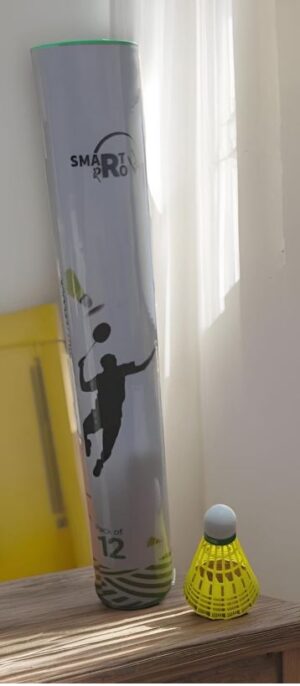 Tall cylindrical box or tube with a badminton player silhouette, labeled 'SMARTRO' beside a yellow shuttlecock holder on a wooden table near a window